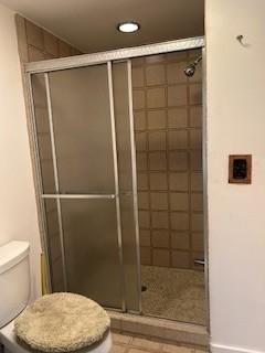 bathroom featuring a shower with door and toilet