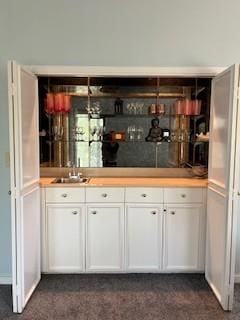 bar with white cabinetry, dark carpet, and sink