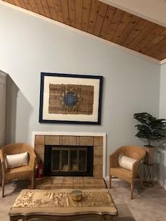 sitting room featuring a tile fireplace, lofted ceiling, light colored carpet, wood ceiling, and crown molding