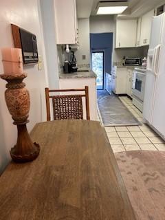 kitchen with range, backsplash, white fridge with ice dispenser, white cabinets, and light tile patterned flooring