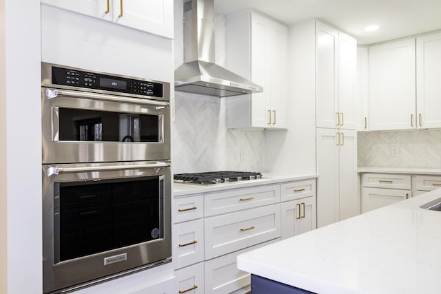 kitchen with white cabinetry, wall chimney exhaust hood, stainless steel appliances, and tasteful backsplash