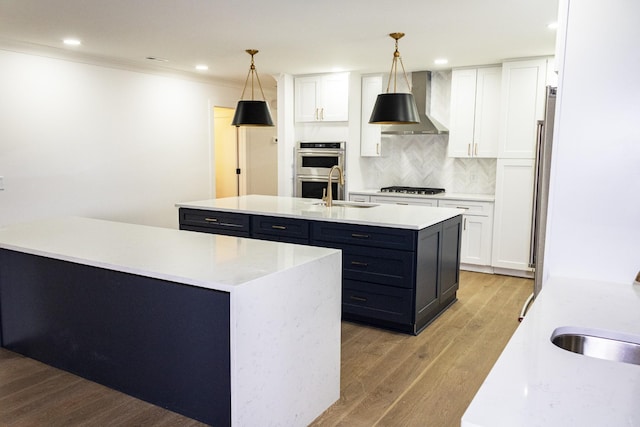 kitchen with pendant lighting, wall chimney exhaust hood, a kitchen island with sink, and white cabinets