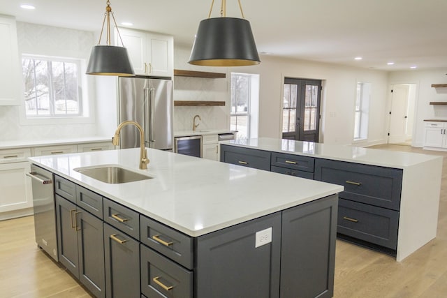 kitchen featuring sink, white cabinetry, high end refrigerator, hanging light fixtures, and a kitchen island with sink