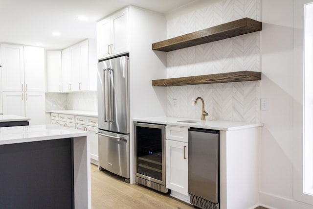 kitchen featuring sink, high end refrigerator, white cabinets, beverage cooler, and light hardwood / wood-style flooring