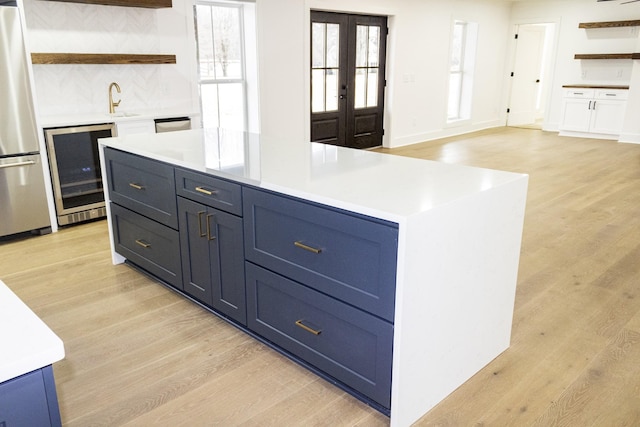 kitchen featuring light hardwood / wood-style flooring, stainless steel refrigerator, backsplash, wine cooler, and blue cabinets