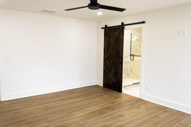 unfurnished room featuring ceiling fan, wood-type flooring, and a barn door