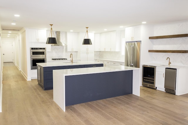 kitchen with wine cooler, appliances with stainless steel finishes, an island with sink, pendant lighting, and white cabinets