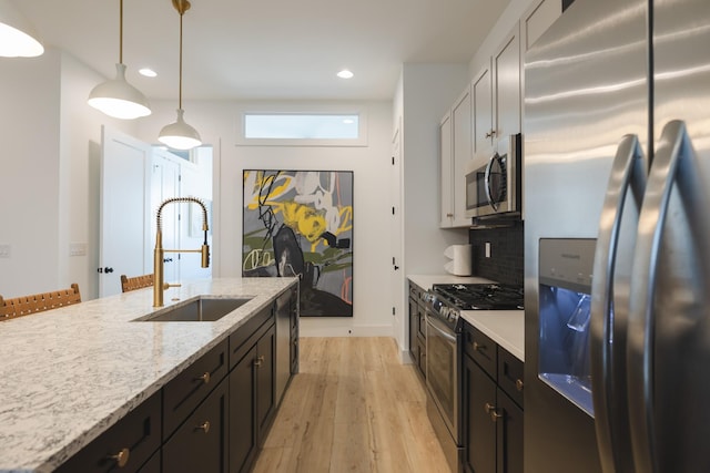 kitchen featuring stainless steel appliances, sink, hanging light fixtures, backsplash, and light stone counters