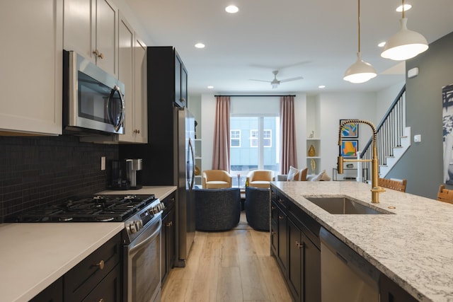 kitchen featuring light stone countertops, decorative light fixtures, stainless steel appliances, sink, and ceiling fan