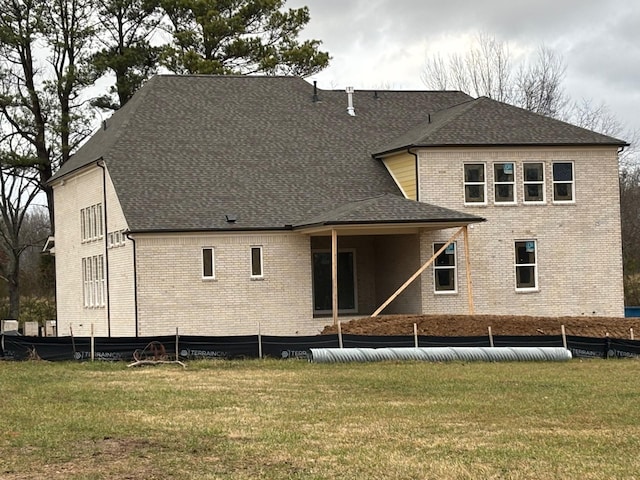 rear view of property featuring a shingled roof, brick siding, and a yard