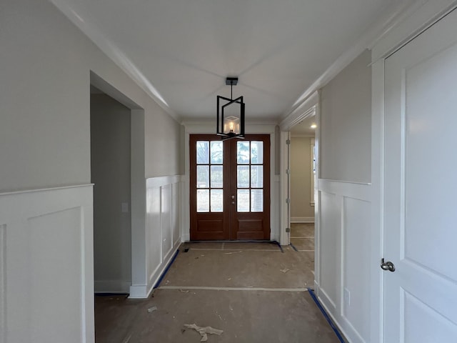 interior space with a wainscoted wall, ornamental molding, a decorative wall, and french doors