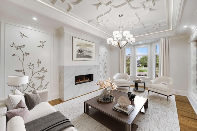 living room with hardwood / wood-style floors, a high end fireplace, ornamental molding, a chandelier, and a raised ceiling