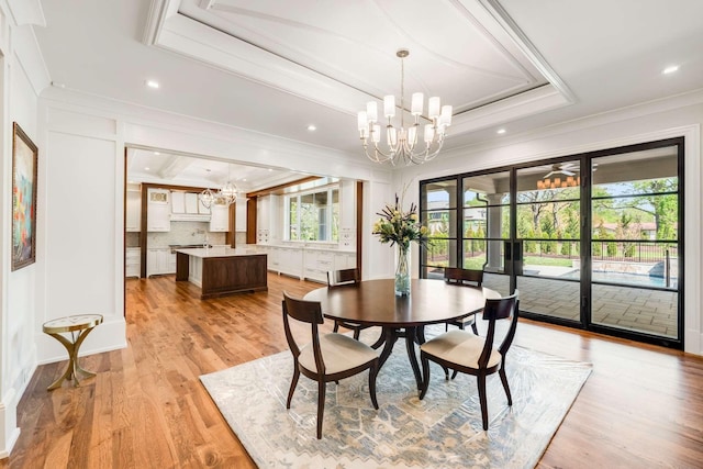 dining room with an inviting chandelier, ornamental molding, a raised ceiling, and light hardwood / wood-style flooring