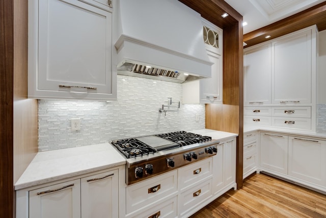 kitchen featuring stainless steel gas stovetop, light hardwood / wood-style floors, backsplash, custom range hood, and white cabinets