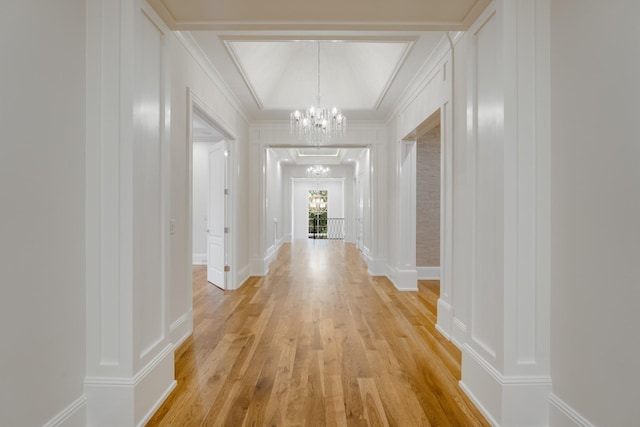 corridor featuring a notable chandelier, ornamental molding, light wood-type flooring, and decorative columns