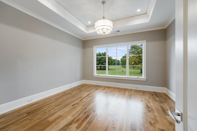 empty room featuring a raised ceiling, an inviting chandelier, ornamental molding, and light hardwood / wood-style floors