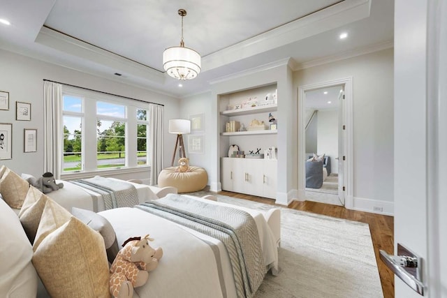 bedroom with a tray ceiling, ornamental molding, a notable chandelier, and light wood-type flooring