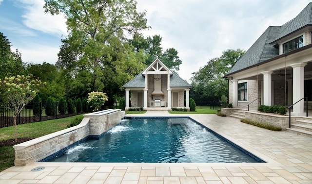 view of swimming pool with a patio area, an outdoor structure, an outdoor stone fireplace, and pool water feature