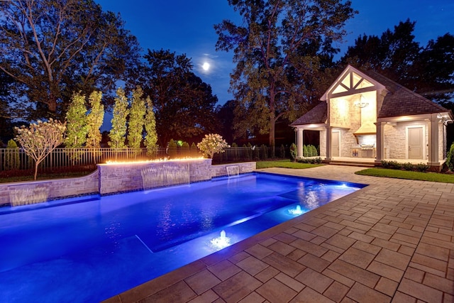 pool at night with pool water feature, an outdoor structure, and a patio