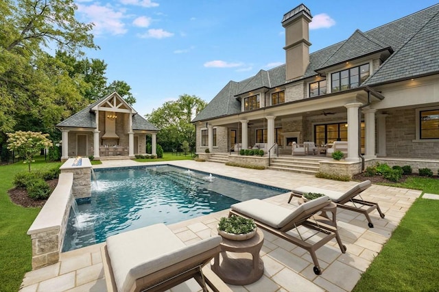 view of pool featuring pool water feature, ceiling fan, a lawn, and a patio