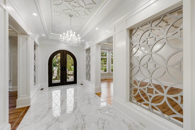 entrance foyer with a chandelier, french doors, a tray ceiling, and ornamental molding