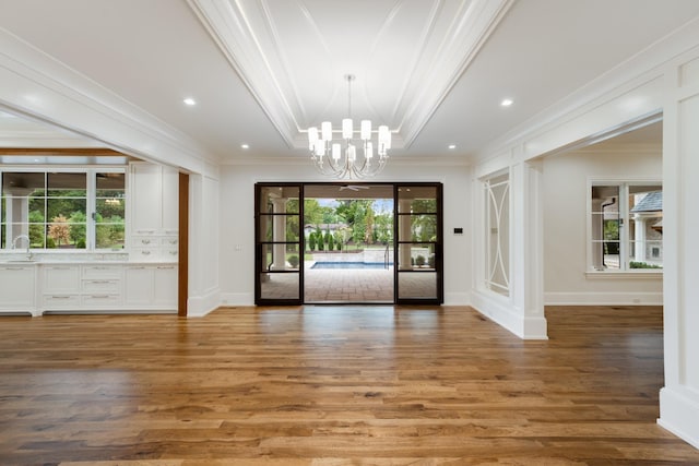 interior space featuring wood-type flooring, an inviting chandelier, sink, a raised ceiling, and ornamental molding