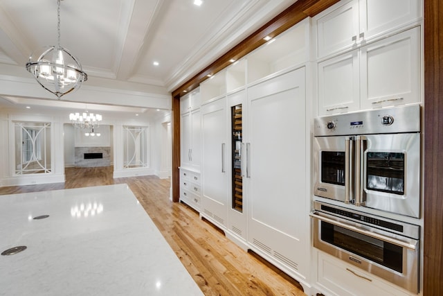 kitchen with stainless steel double oven, white cabinetry, hanging light fixtures, a chandelier, and beam ceiling