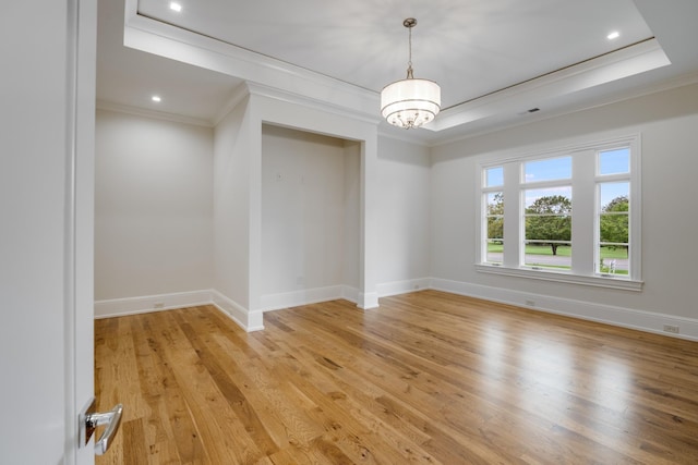 spare room with a raised ceiling, an inviting chandelier, crown molding, and light hardwood / wood-style flooring