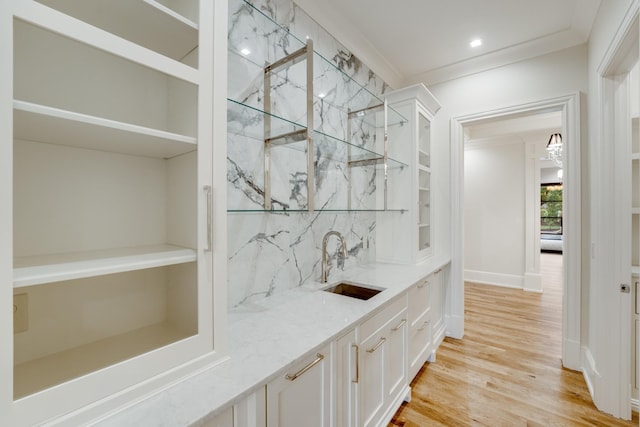 bar featuring white cabinets, crown molding, light hardwood / wood-style flooring, light stone counters, and sink