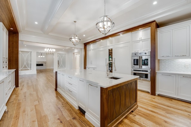 kitchen with sink, pendant lighting, white cabinetry, and a center island with sink