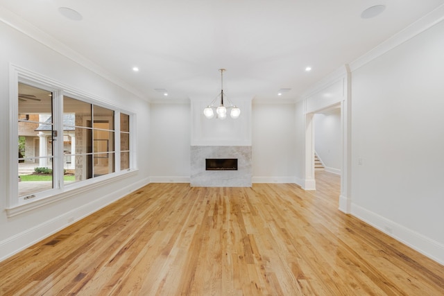 unfurnished living room featuring light wood-type flooring, crown molding, a fireplace, and a notable chandelier