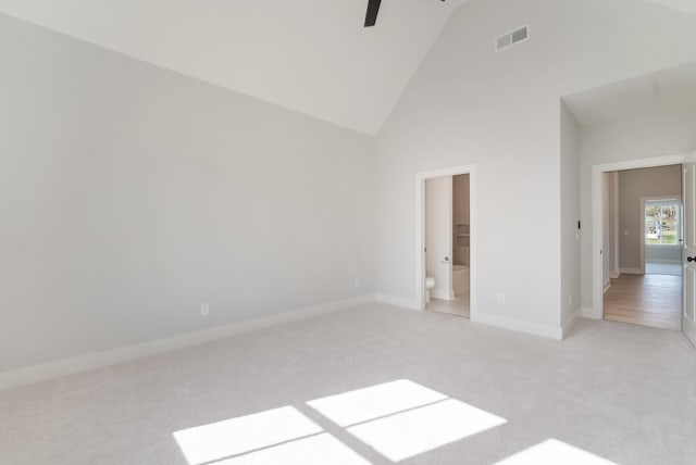 unfurnished bedroom with high vaulted ceiling, light colored carpet, ensuite bath, and ceiling fan