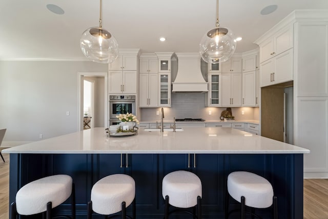 kitchen with sink, light hardwood / wood-style floors, a spacious island, and custom range hood