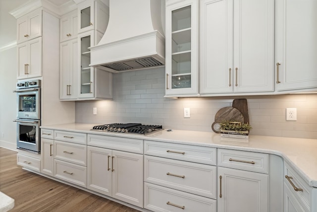 kitchen featuring premium range hood, appliances with stainless steel finishes, backsplash, and white cabinetry