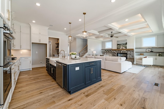 kitchen featuring ceiling fan, decorative light fixtures, a center island with sink, blue cabinetry, and white cabinets