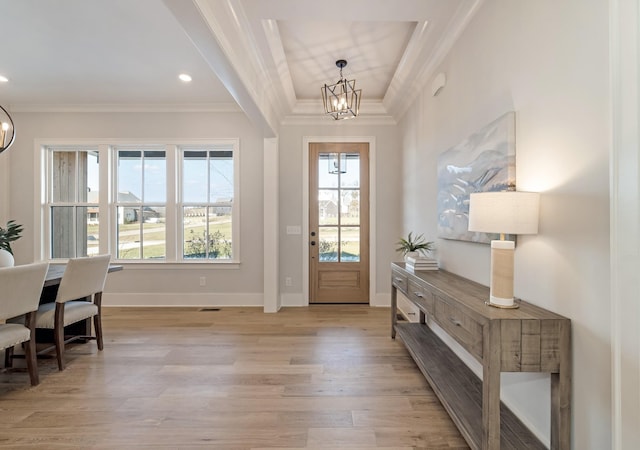 entrance foyer featuring light wood-type flooring, an inviting chandelier, ornamental molding, and a raised ceiling