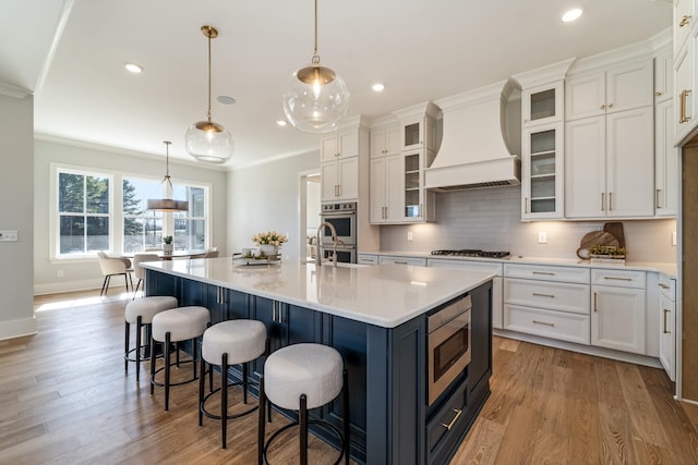 kitchen featuring premium range hood, pendant lighting, a center island with sink, and stainless steel appliances