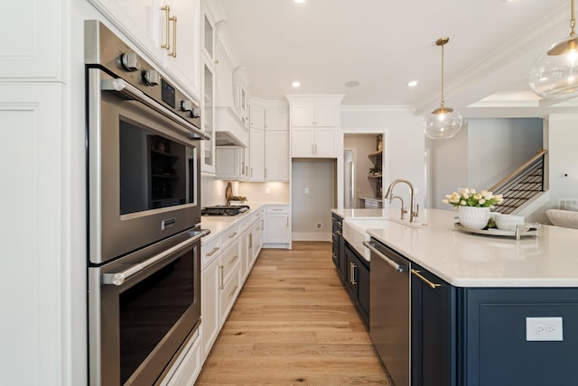 kitchen with pendant lighting, white cabinets, appliances with stainless steel finishes, sink, and crown molding