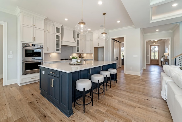 kitchen featuring decorative light fixtures, double oven, premium range hood, and white cabinetry