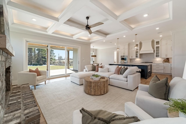 living room featuring ceiling fan, a brick fireplace, light hardwood / wood-style floors, beam ceiling, and coffered ceiling