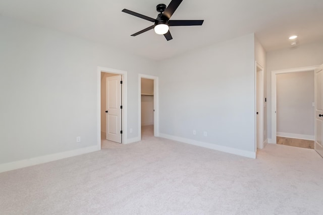 unfurnished bedroom with ceiling fan, a walk in closet, a closet, and light carpet