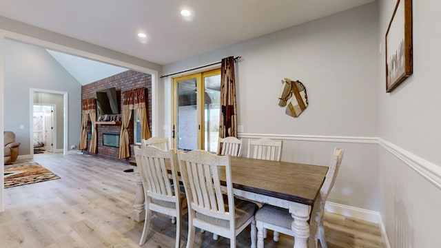 dining space featuring a brick fireplace, lofted ceiling, and light hardwood / wood-style flooring