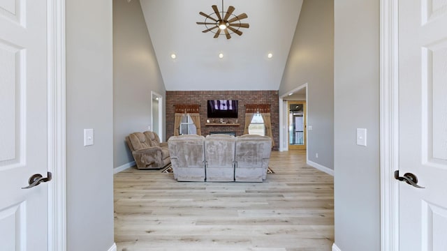 living room featuring ceiling fan, light hardwood / wood-style floors, high vaulted ceiling, and a brick fireplace