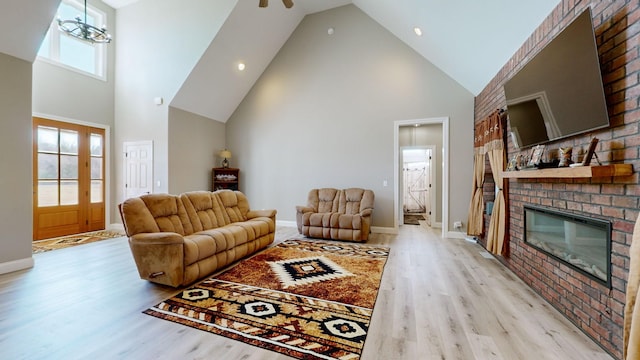 living room featuring high vaulted ceiling, a brick fireplace, ceiling fan with notable chandelier, and light hardwood / wood-style floors