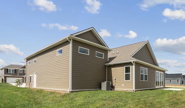 rear view of house featuring central AC unit, a garage, and a lawn