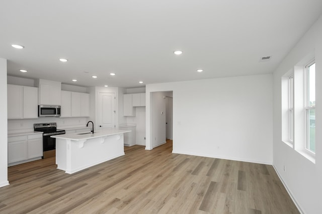 kitchen featuring appliances with stainless steel finishes, white cabinetry, an island with sink, sink, and light hardwood / wood-style flooring