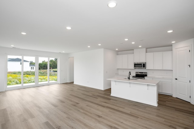 kitchen featuring white cabinets, appliances with stainless steel finishes, light hardwood / wood-style floors, sink, and a center island with sink