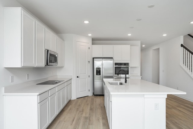 kitchen with sink, white cabinets, stainless steel appliances, a center island with sink, and light hardwood / wood-style flooring