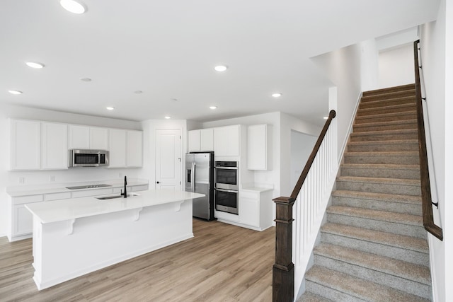 kitchen featuring a breakfast bar, white cabinetry, appliances with stainless steel finishes, a kitchen island with sink, and light hardwood / wood-style floors