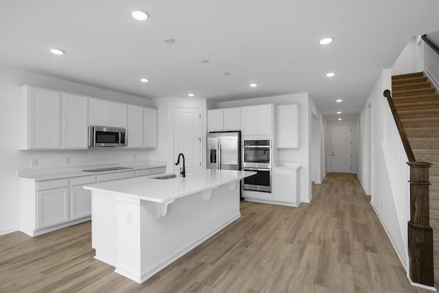 kitchen with sink, appliances with stainless steel finishes, white cabinets, a center island with sink, and light wood-type flooring